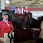 A woman standing next to two horses in a barn.