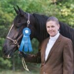 A woman in brown jacket holding a horse.