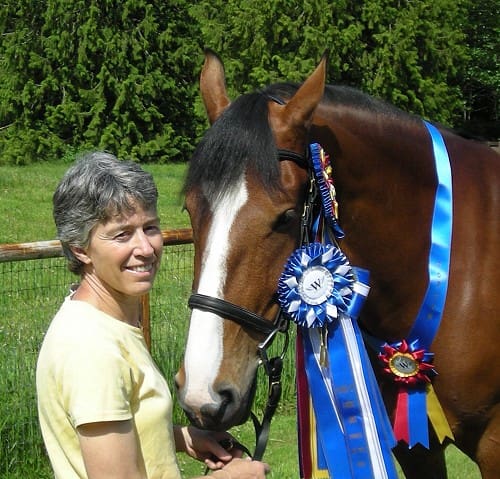 A person stands beside a horse adorned with multiple blue and red ribbons, indicating awards or prizes.