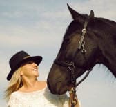 A woman wearing a black hat smiles at a black horse.