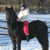 A child in a helmet and winter clothing rides a black horse in a snowy field near a wooden fence. Date on the image reads 12/30/2022.